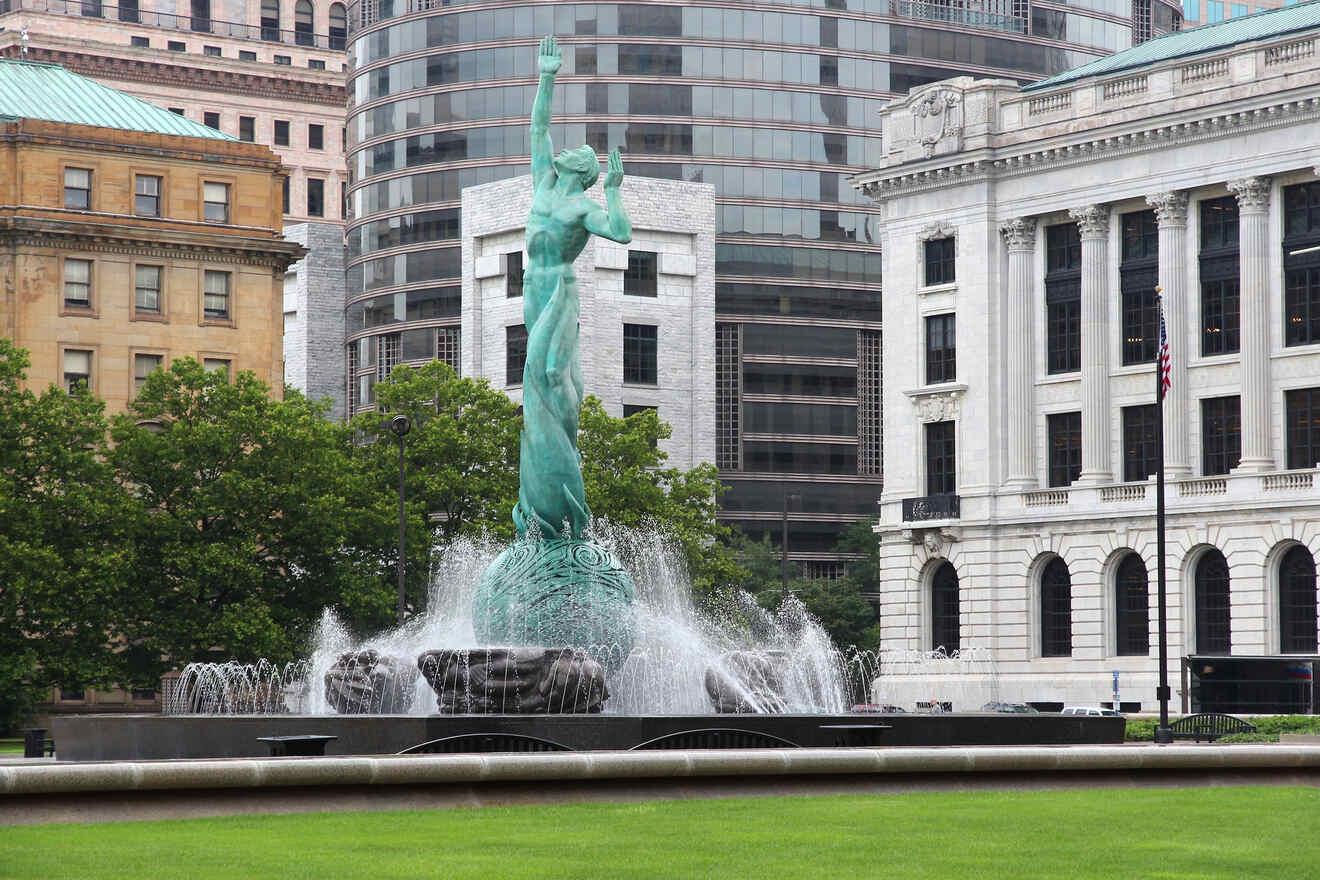A fountain statue with outstretched arms in front of classic and modern architecture, symbolizing peace and city pride.